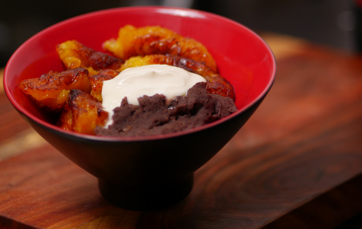 A bowl of refried beans, fried plantains and sour cream