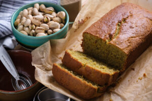 A pistachio and cardamon loaf that's been sliced twice sitting atop parchment paper.