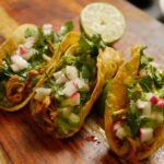 Three chicken tacos side by side on a cutting board.
