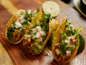 Three chicken tacos side by side on a cutting board.